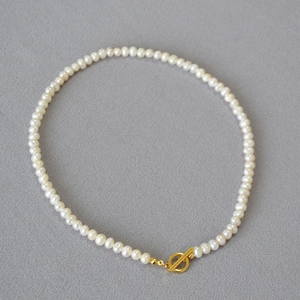 Macro shot of freshwater pearl necklace with gold OT toggle clasp on textured gray fabric
