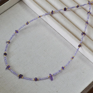 Detail of amethyst beaded necklace with purple stones and gold accents on velvet tray