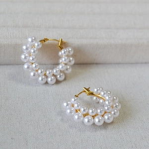 Elegant French vintage style pearl hoop earrings with gold base on soft fabric background