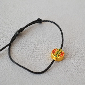 Detail of brass gold-plated charm on black cord bracelet with red and green enamel patterns