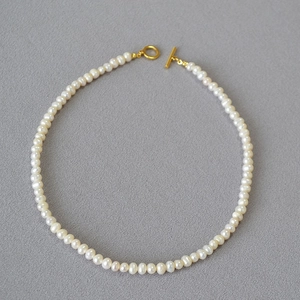 Elegant Baroque freshwater pearl necklace with a golden OT toggle clasp on grey linen