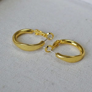 Minimalist twisted geometric gold hoop earrings with 925 silver needles on linen