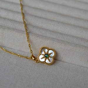 Macro du collier trèfle doré avec nacre blanche et détail d'étoile en zircone verte