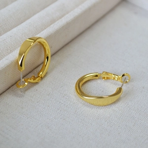 Macro shot of minimalist gold geometric hoop earrings on a beige textured fabric background