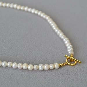 Detailed macro view of white freshwater pearls and golden OT toggle clasp on a necklace