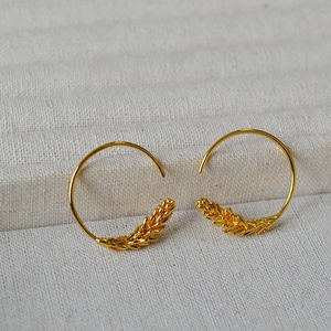 Detailed close-up of golden wheat ear hoop earrings on cream textured fabric