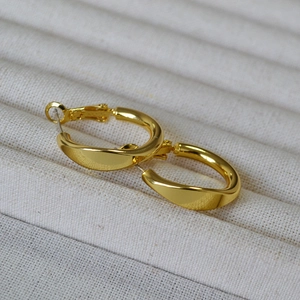 Minimalist gold twisted hoop earrings with a polished finish on a white jewelry display