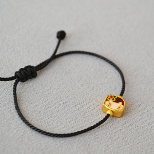 Detail of black woven rope bracelet with gold enamel doll charm and adjustable clasp