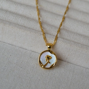Collier rose doré avec pendentif en nacre irisante sur boîte à bijoux beige