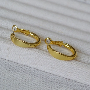 Macro shot of minimalist gold oval hoop earrings with mirror finish on textured fabric