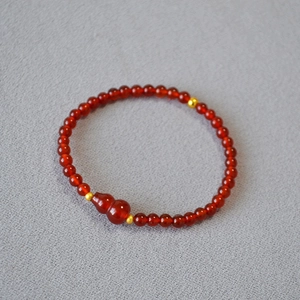 Dettaglio del bracciale di agata rossa con ciondolo hulu e perline distanziatrici d'oro