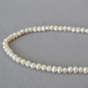 Macro shot of lustrous cream freshwater pearls on textured grey fabric necklace detail