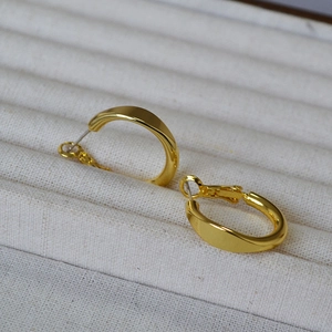 Detailed view of minimalist gold geometric hoop earring on a cream jewelry tray