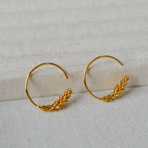 Macro detail of gold-plated geometric hoop earrings with intricate wheat ear grain texture