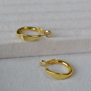 Minimalist thick gold twisted hoop earrings with a glossy finish on textured fabric