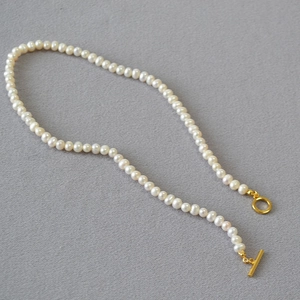 Detail of freshwater pearl necklace featuring a golden OT toggle clasp on textured fabric