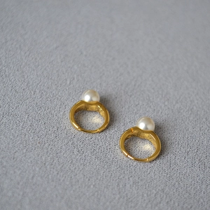 Boucles d'oreilles créoles dorées avec perles blanches sur fond en tissu gris