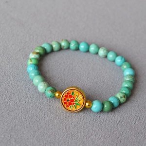 Detail of turquoise beaded bracelet with golden floral enamel charm on gray fabric