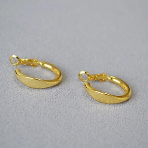 Detail of high-polished gold oval hoop earrings on light grey textured background