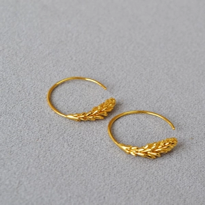 Macro detail of gold wheat ear hoop earrings with fine textures on neutral fabric
