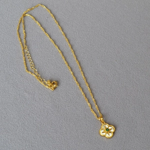 Détail du collier trèfle doré avec incrustation en nacre et une pierre précieuse verte