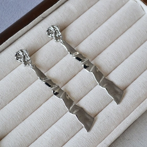 Polished silver wave drop earrings with irregular crinkle texture on jewelry box