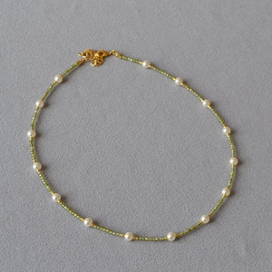 Detail of beaded necklace with green gemstones, white pearls, and golden lobster clasp