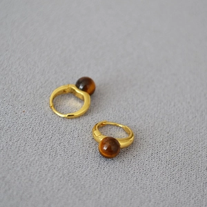 Détail macro de boucles d'oreilles créoles dorées avec pierre brune sur tissu gris