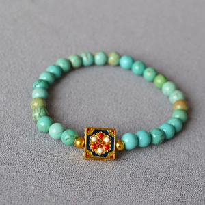 Macro detail of turquoise beaded bracelet with floral enamel cloisonné square charm