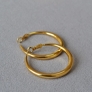 Macro detail of large gold-plated hoop earrings with polished mirror finish on fabric