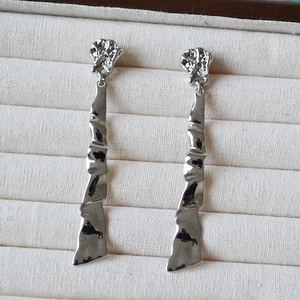 Macro detail of silver-plated crinkled metal wave drop earrings on beige velvet