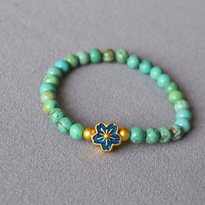 Detailed close-up of beaded turquoise bracelet with golden floral pendant on gray fabric