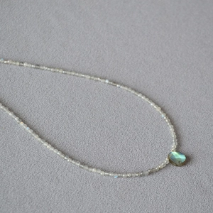 Macro shot of a teardrop labradorite pendant on a beaded grey moonstone necklace