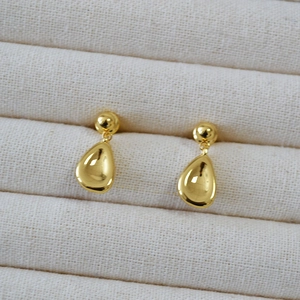 Macro shot of polished gold water drop earrings resting on a beige fabric jewelry box