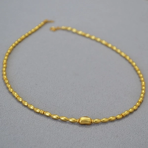 Detail of matte gold baroque beaded necklace featuring a central bean-shaped accent bead