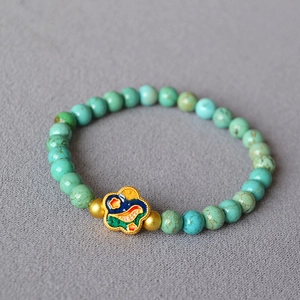 Close-up of vintage turquoise bead bracelet with colorful floral enamel charm and gold spacers