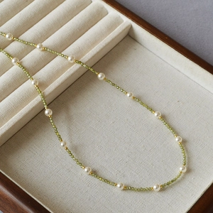 Detail of green zircon beaded necklace with white pearls and gold spacers on linen