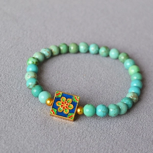 Detailed shot of turquoise bead bracelet with enamel floral charm and golden spacers