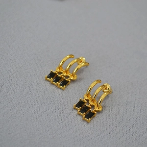 Detailed macro view of gold tassel earrings featuring three rectangular black zircons