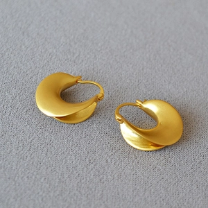 Detail of matte gold geometric crescent earrings with textured brushed metal finish