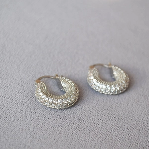 Macro shot of silver hoop earrings fully paved with sparkling cubic zirconia on fabric