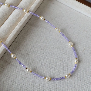 Detailed macro shot of purple faceted beads, white pearls, and gold spacers necklace
