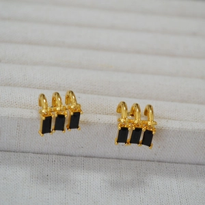 Detail view of gold tassel earrings featuring rectangular black zircon stones on white tray