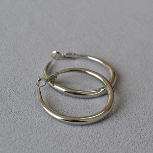 Detailed view of polished silver hoop earrings with a mirror finish on grey fabric
