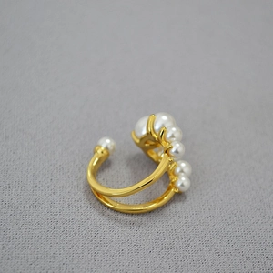 Dettaglio ravvicinato dell'anello aperto in ottone dorato con eleganti perle bianche