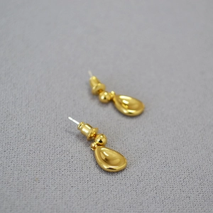 Polished gold teardrop dangle earrings on grey textured fabric background for women