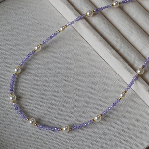 Detail of beaded necklace with purple faceted stones, white pearls, and gold spacers