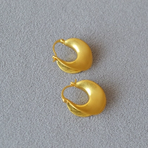 Detail of chunky gold crescent earrings with a textured matte finish on grey fabric