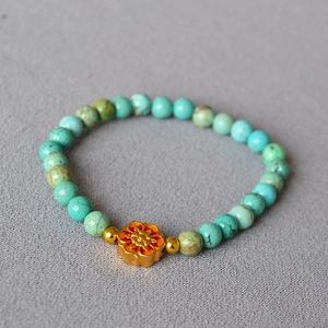 Macro detail of turquoise beaded bracelet featuring a golden floral brass pendant