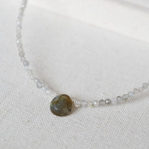 Macro shot of faceted grey beads and a teardrop labradorite pendant on a linen surface